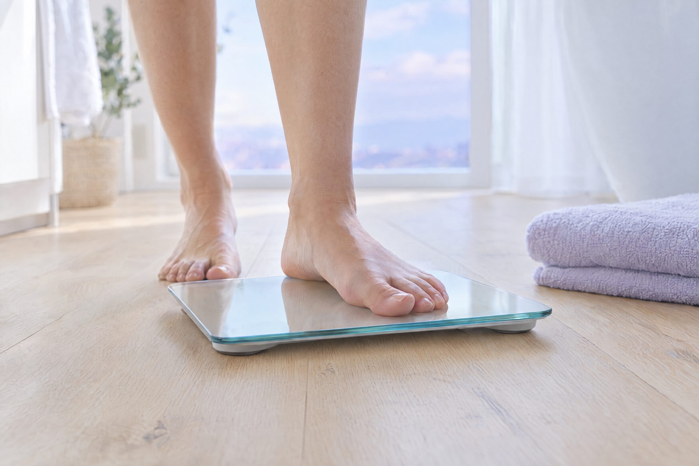 Bare feet stepping onto a slim glass scale on a wooden floor