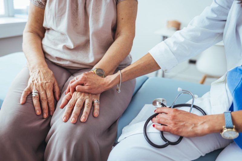 A doctor holding a senior patient's hand in a bright care setting