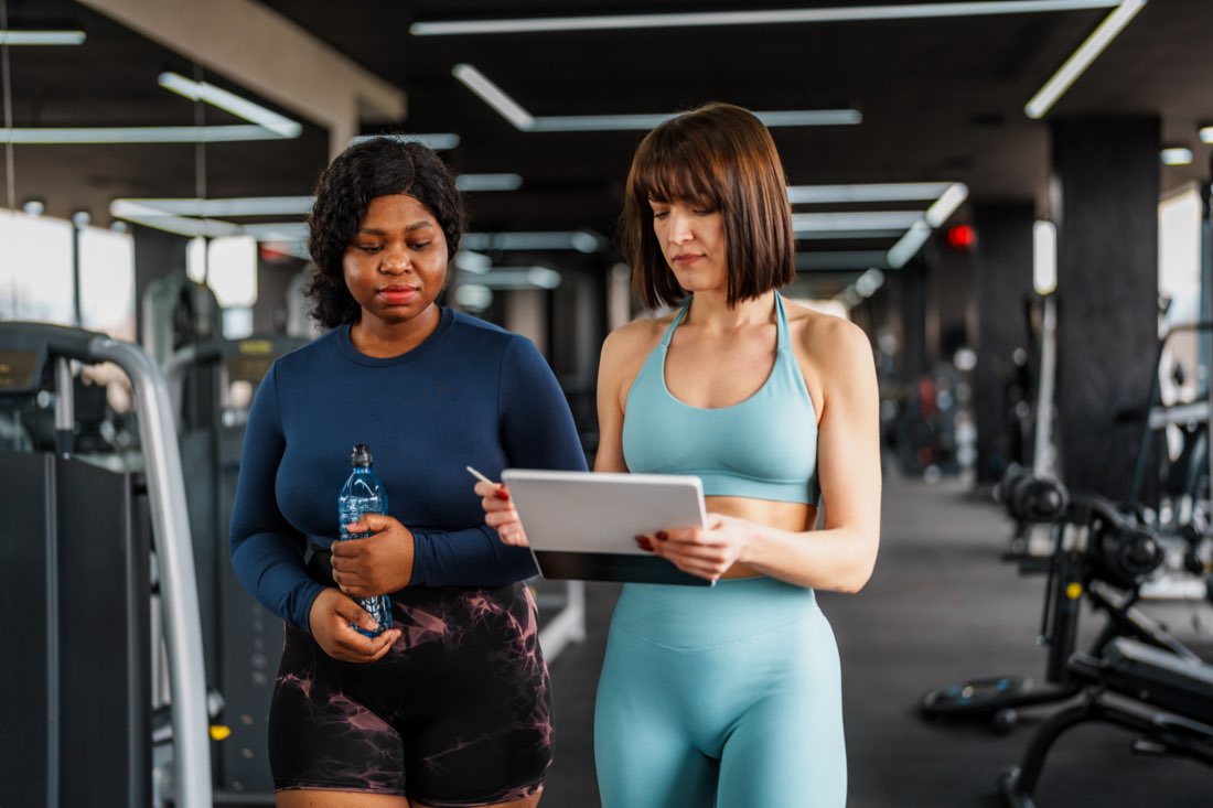 A trainer and client reviewing a fitness plan on a tablet in a gym